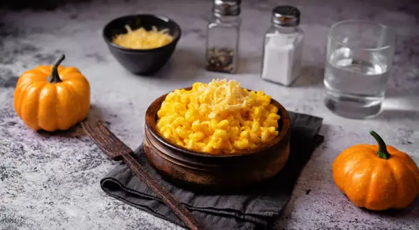 Un invitante piatto di pasta e zucca, guarnito con formaggio grattugiato, accanto a piccole zucche arancioni.