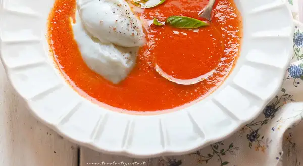 Una cremosa zuppa di pomodoro, arricchita da due quenelle di burrata e foglie di basilico fresco. Un piatto invitante e gustoso.