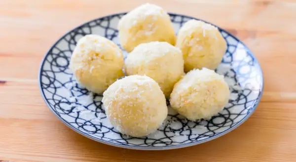 Piatto con dolcetti al cocco, soffici e bianchi, su un fondo di legno.