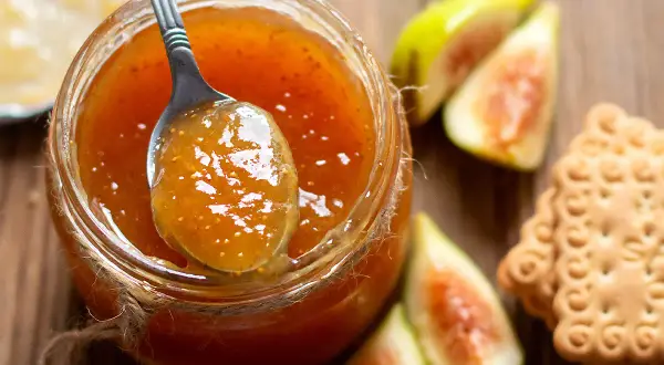 Un cucchiaio raccoglie la deliziosa marmellata di fichi da un barattolo, accanto a fichi freschi e biscotti.