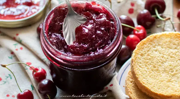 Un barattolo pieno di marmellata di ciliegie fatta in casa, con ciliegie fresche e fette biscottate.