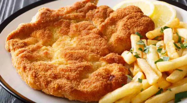 Cotoletta alla milanese dorata e croccante, servita con patatine fritte e spicchi di limone.