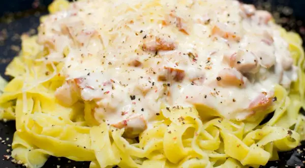 Pasta fresca condita con una cremosa salsa bianca e pezzetti di prosciutto crudo, cosparsa di parmigiano e pepe nero.