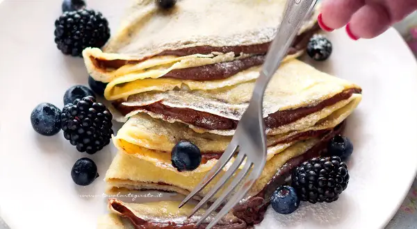 Piatto di crepes alla Nutella, guarnite con mirtilli e more, pronte per essere gustate.