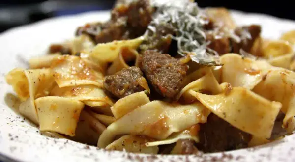 Pappardelle al cinghiale fumanti, con pezzi di carne succulenta e una spolverata di parmigiano.