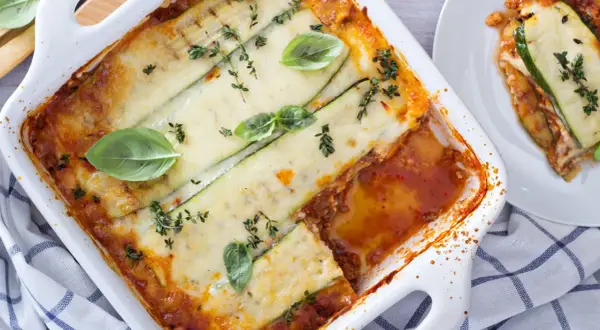 Lasagne di zucchine al forno, dorate e filanti, guarnite con basilico fresco e timo. Un piatto leggero e gustoso.