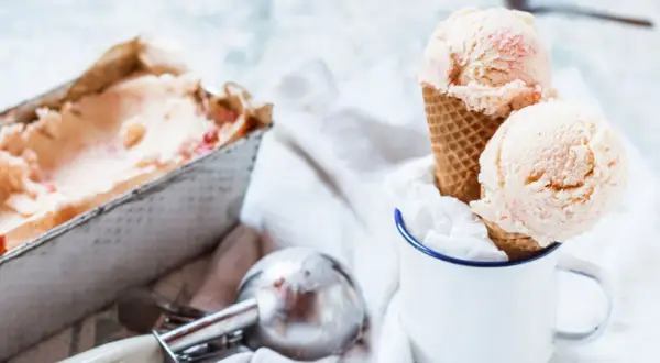 Due palline di gelato fatto in casa, con pezzetti di frutta, in un cono, accanto a una vaschetta e un porzionatore.
