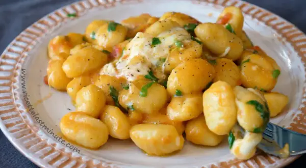 Gnocchi di spinaci cremosi con formaggio filante e prezzemolo fresco, serviti su un piatto decorato.