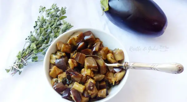 Melanzane in padella, un contorno saporito, con un mazzetto di erbe aromatiche e una melanzana intera.