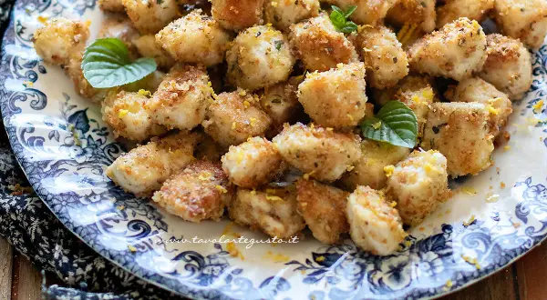 Bocconcini di pollo dorati e croccanti, guarniti con scorza di limone e foglioline di menta, su un piatto decorato.