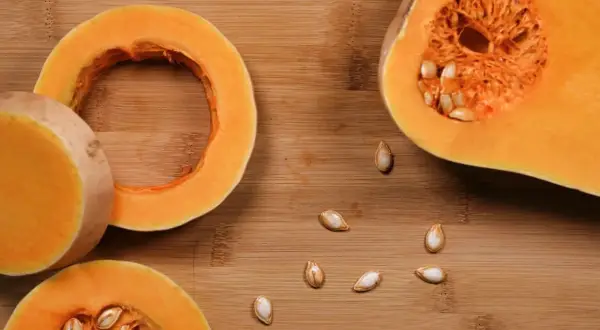 Fette di zucca pronte per essere cotte in padella, con semi sparsi sul tagliere di legno.