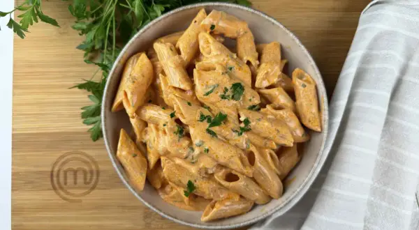 Penne alla vodka cremose e invitanti, guarnite con prezzemolo fresco, su un tagliere di legno con il logo di MasterChef.