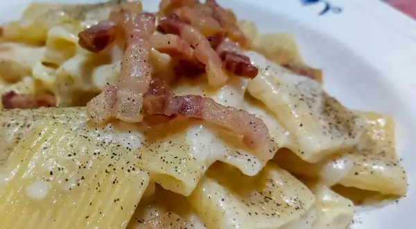 Un piatto di pasta alla gricia fumante, con guanciale croccante e abbondante pepe nero.