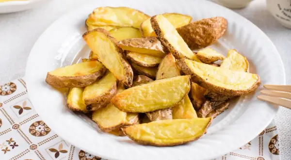 Patate a spicchi dorate e croccanti, appena sfornate dalla friggitrice ad aria, servite su un piatto bianco.
