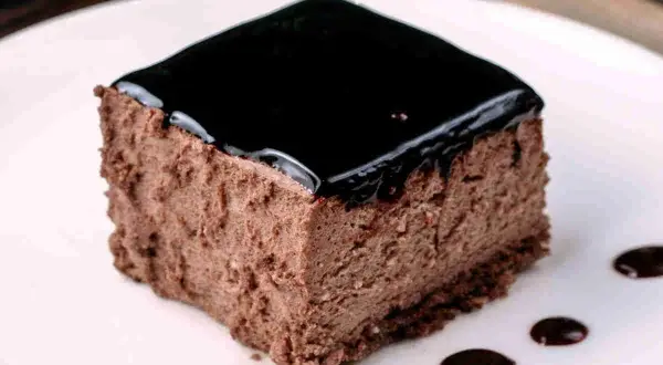 Un delizioso semifreddo al cioccolato, con una lucida glassa scura e gocce di salsa al cioccolato sul piatto bianco.