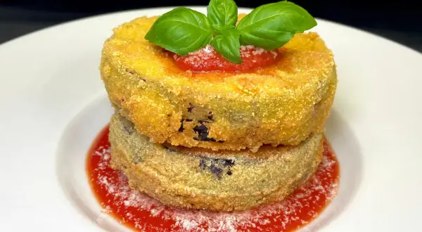 Due cordon bleu di melanzane impilati, dorati e croccanti, su salsa di pomodoro e basilico fresco.