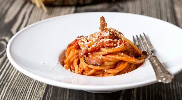 Un piatto di spaghetti alla amatriciana, con guanciale croccante e una salsa rossa saporita. La cipolla, ingrediente chiave della ricetta originale, dona un tocco in più.