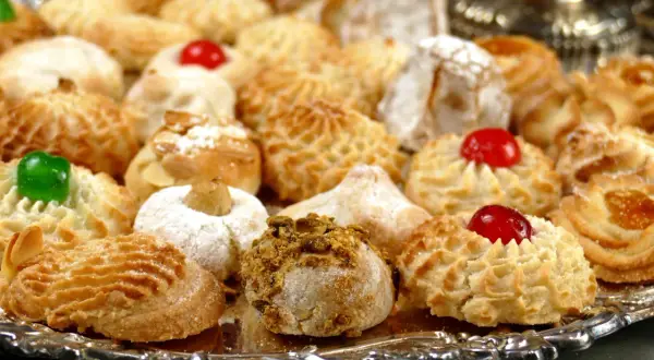 Vassoio pieno di biscotti alle mandorle morbidi, alcuni decorati con ciliegie candite, mandorle e pistacchi.