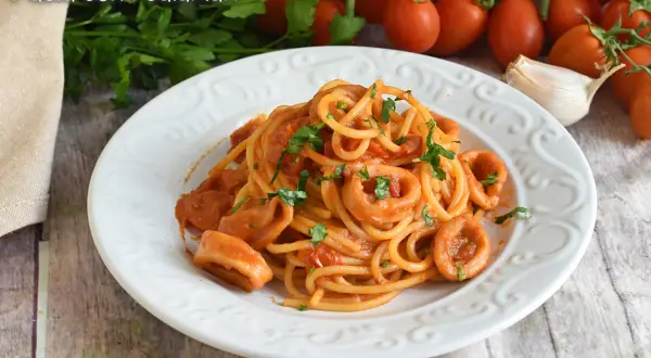 Un piatto di spaghetti con anelli di calamari e pomodoro, guarnito con prezzemolo fresco.