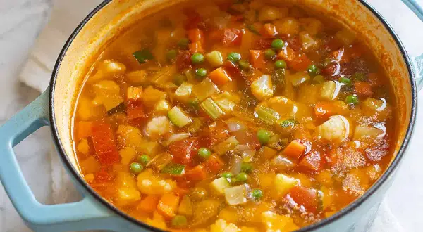 Un fumante minestrone di verdure in una pentola azzurra, ricco di carote, zucchine, piselli e cavolfiore.