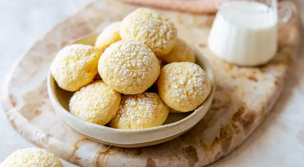 Una ciotola piena di biscotti da inzuppo spolverati di zucchero a velo, pronti per essere gustati con un bicchierino di latte.