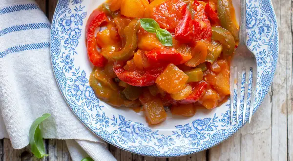 Un piatto di peperonata con patate, colorato e invitante, guarnito con basilico fresco.