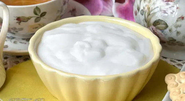 Una ciotola gialla piena di soffice crema al latte, accanto a una tazza di tè e fiori.