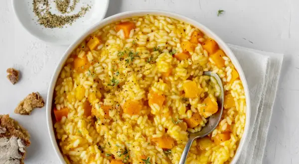 Un cremoso risotto con la zucca, guarnito con timo fresco e pepe nero macinato. Accanto, pane rustico e una ciotolina di pepe.