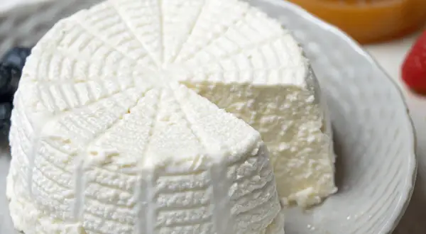 Ricotta fatta in casa, fresca e cremosa, servita su un piatto con mirtilli e fragole.