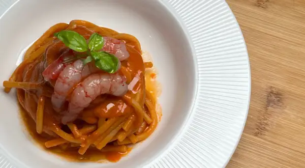 Spaghetti al sugo di pomodoro con gamberi freschi e basilico, un piatto che evoca il sapore intenso della bisque di gamberi.