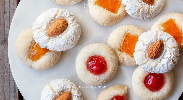 Biscotti alla pasta di mandorle con mandorle intere, marmellata d'arancia e ciliegie candite, spolverati di zucchero a velo.