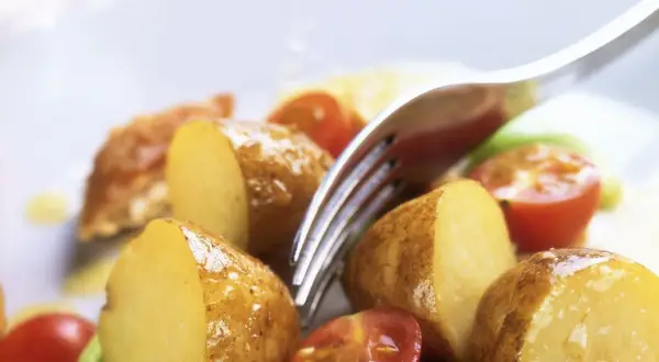 Patate novelle tagliate a metà, pomodorini e un tocco di verde compongono questa fresca insalata di patate estiva, pronta per essere gustata.
