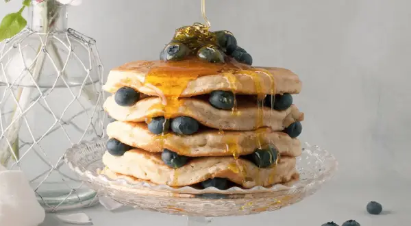 Pancake senza latte, una torre dorata con mirtilli freschi e sciroppo d'acero che cola. Delizioso e leggero, perfetto per ogni momento.