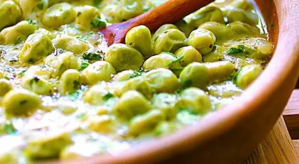 Un primo piatto saporito: piselli in umido, cremosi e profumati, serviti in una ciotola di legno con un cucchiaio.