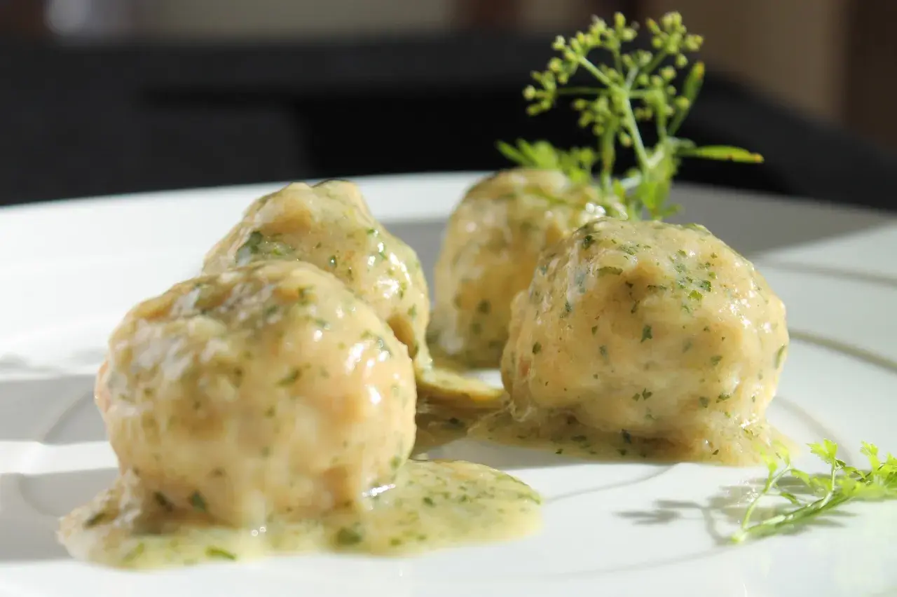 Quattro polpette in bianco su un piatto bianco, condite con una salsa cremosa e erbe aromatiche.