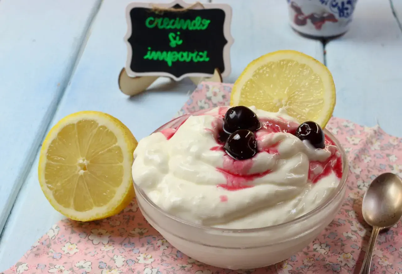 Deliziosa mousse al limone con ciliegie e una fetta di limone, servita in una ciotola su un tovagliolo fiorato.