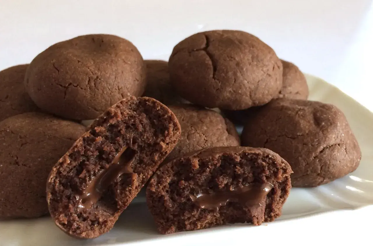 Biscotti al cioccolato morbidi con cuore filante. Alcuni sono interi, altri spezzati per mostrare il ripieno goloso.