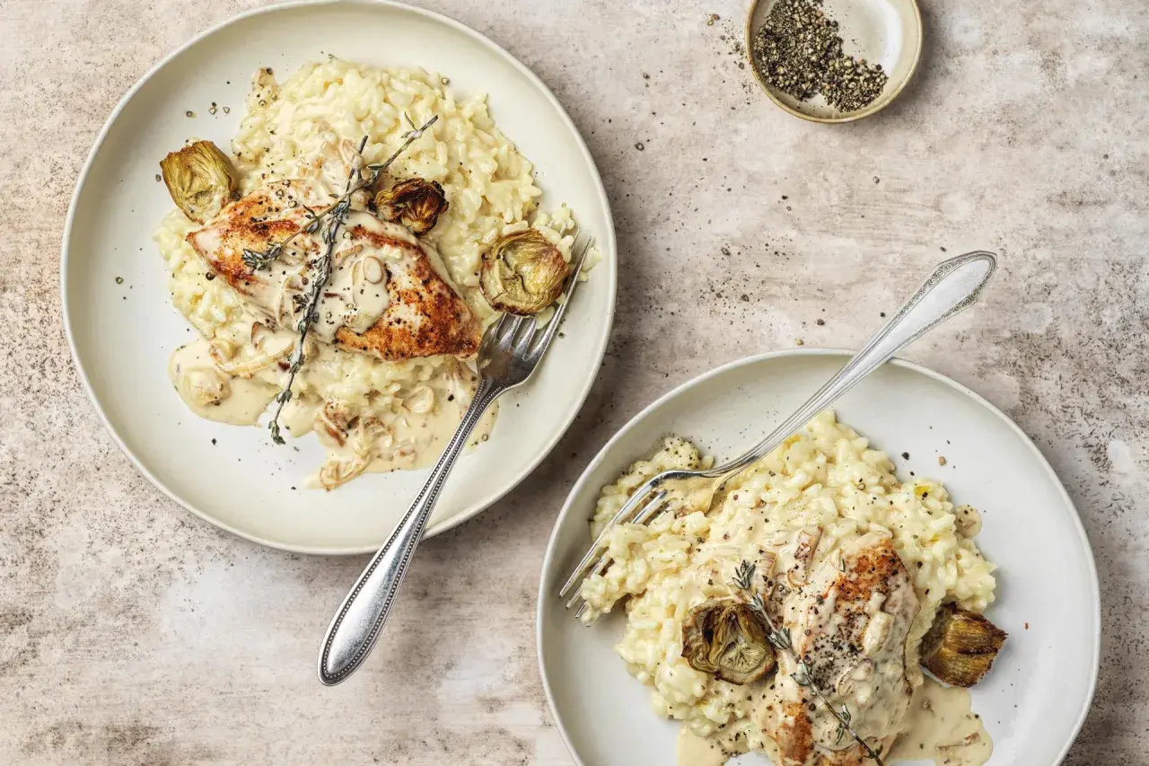 Due piatti di cremoso riso con pollo, guarniti con carciofi e rosmarino. Un piatto invitante e saporito.