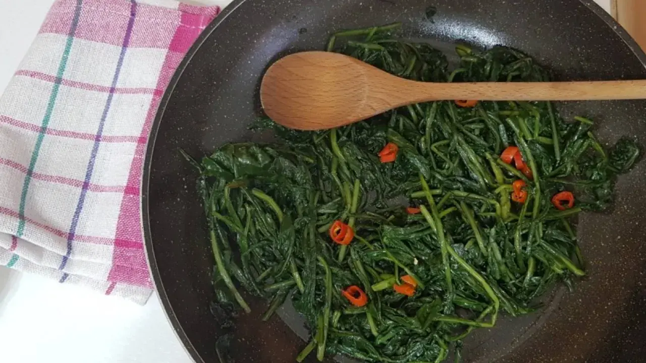 Cicoria in padella, un contorno saporito con peperoncino e un cucchiaio di legno pronto a mescolare.