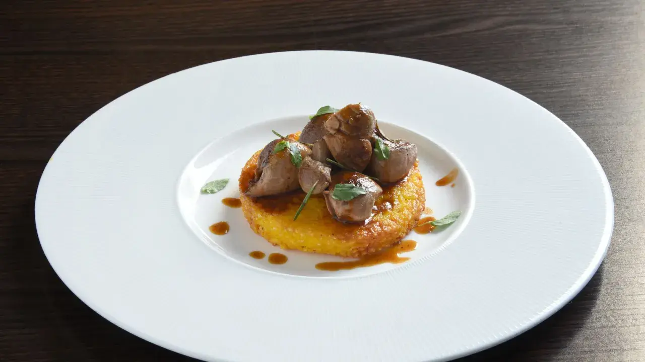 Delizioso riso al salto con bocconcini di carne e salsa bruna, guarnito con erbe fresche su un piatto bianco.