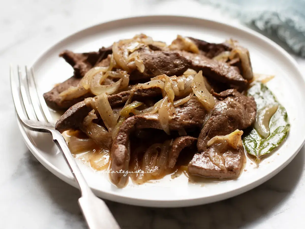 Piatto di fegato alla veneziana con cipolle caramellate, servito su un piatto bianco con una forchetta.