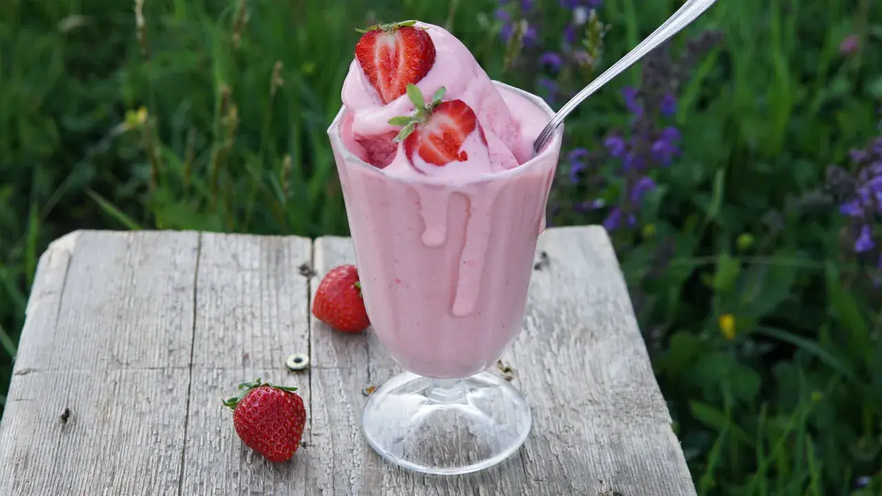 Un bicchiere di cremoso gelato alla fragola, guarnito con fragole fresche, su un tavolo di legno rustico.