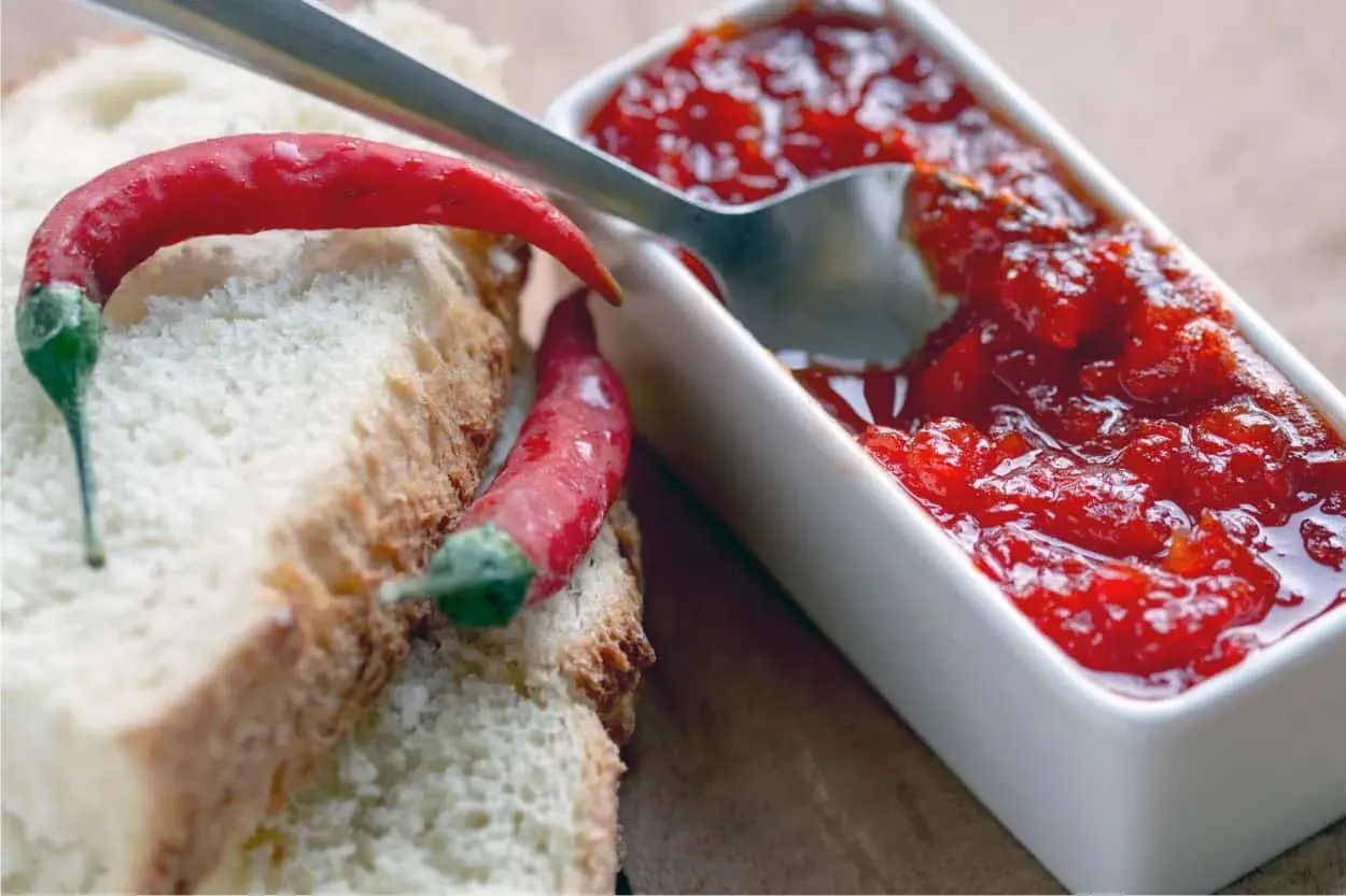 Fette di pane con peperoncini rossi e una ciotolina di marmellata di peperoncino, pronta per essere gustata.