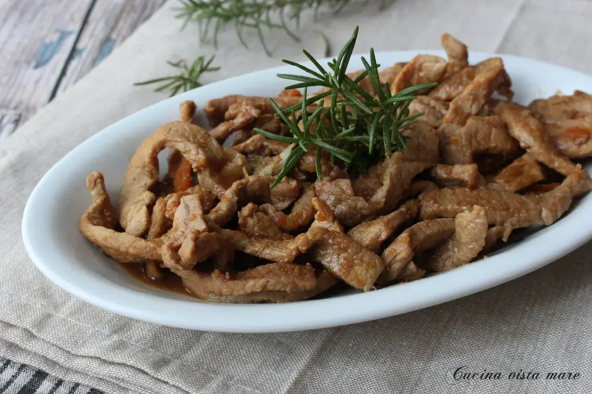 Deliziosi straccetti di vitello saltati, guarniti con rosmarino fresco, serviti in un piatto bianco su un tovagliolo di lino.