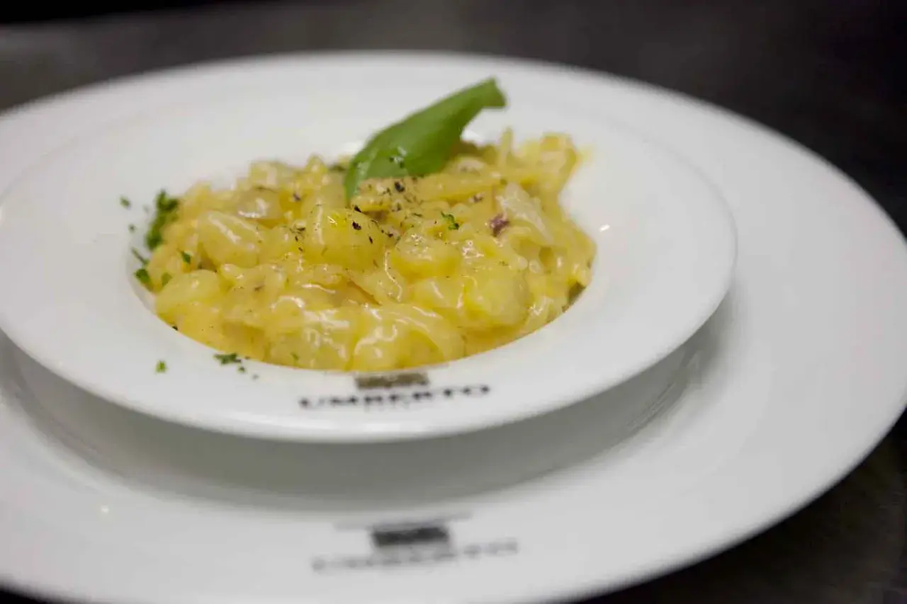 Un piatto di pasta e patate cremoso, guarnito con basilico fresco e pepe nero, servito in un elegante piatto bianco.