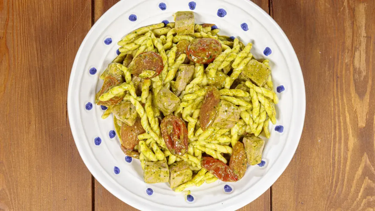 Piatto di trofie alla carlofortina con tonno, pomodorini secchi e pesto, servito su un piatto bianco con decorazioni blu.