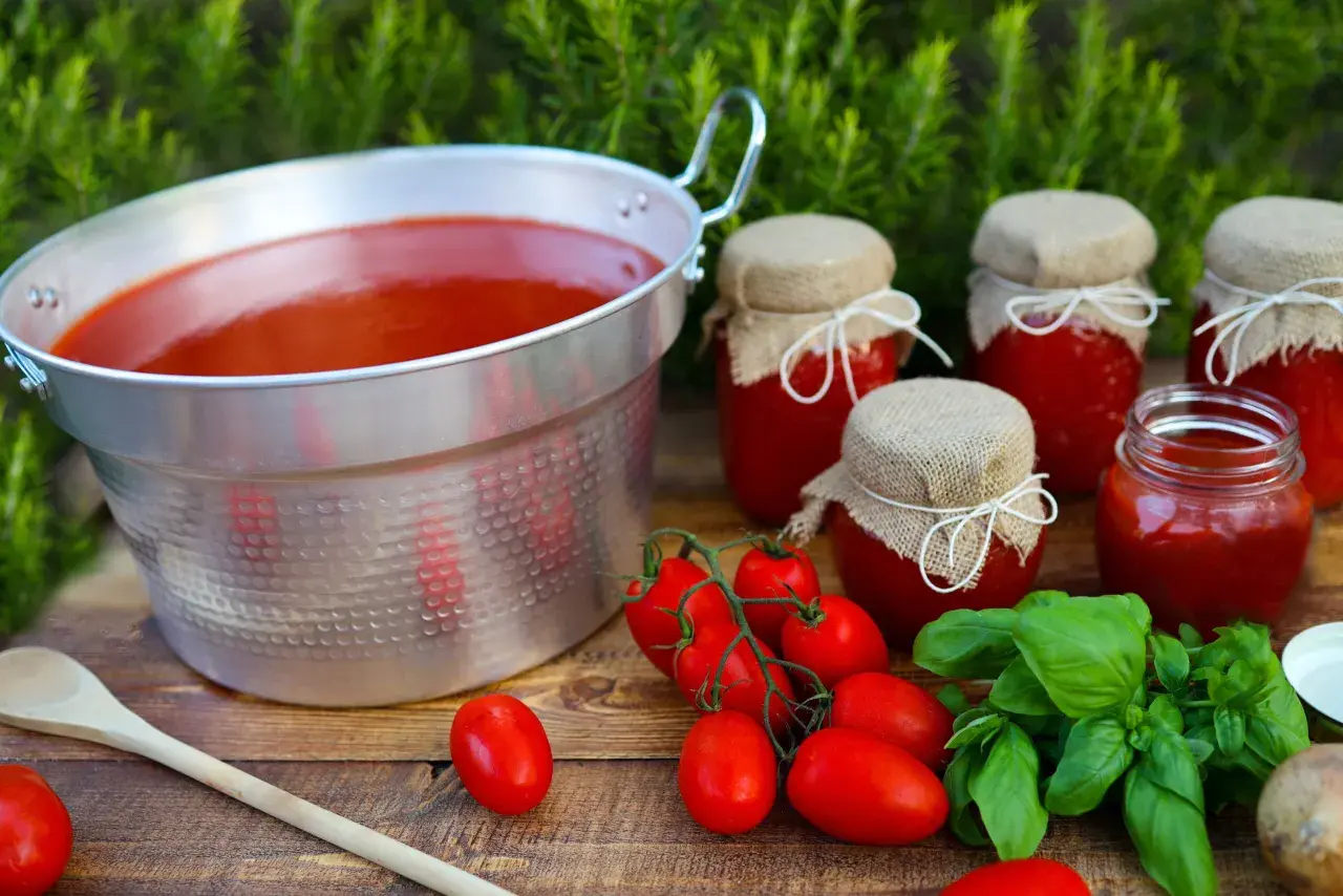 Un grande pentolone di passata di pomodoro, vasetti fatti in casa e pomodori freschi, pronti per la conservazione.