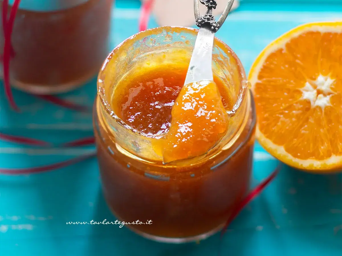 Un vasetto di marmellata di arance fatto in casa, con una fetta d'arancia accanto. La marmellata è lucida e invitante, pronta per essere gustata.