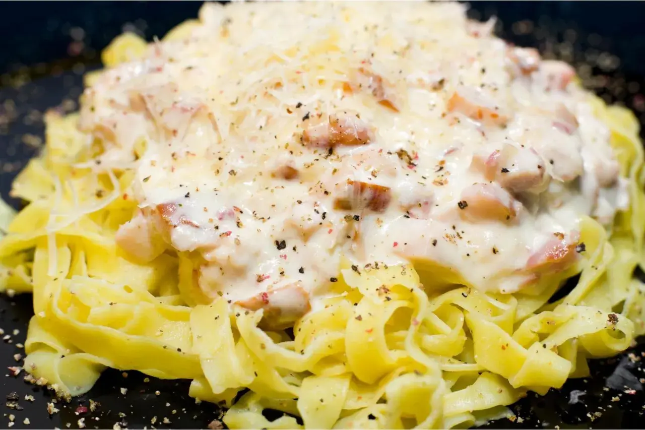 Pasta fresca condita con una cremosa salsa bianca e pezzetti di prosciutto crudo, cosparsa di parmigiano e pepe nero.