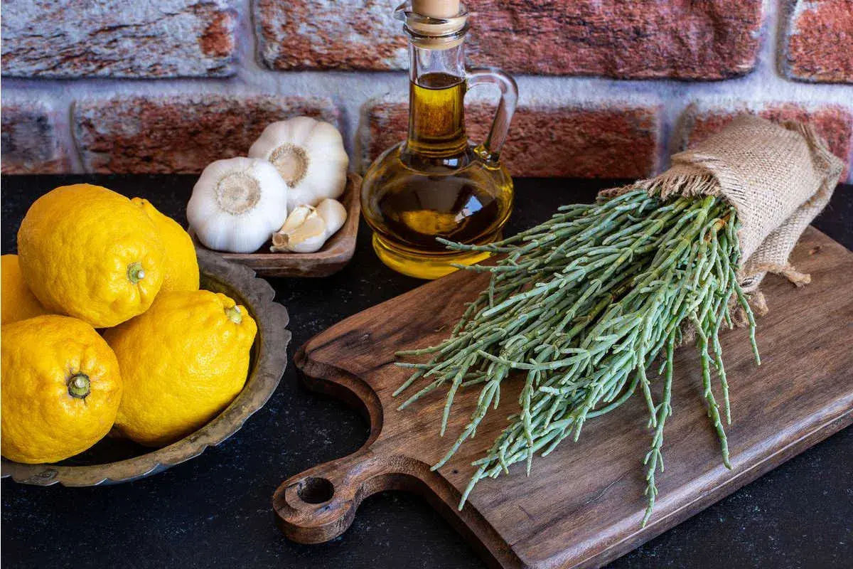 Asparagi di mare freschi, limoni, aglio e olio d'oliva su un tagliere di legno, pronti per una ricetta saporita.